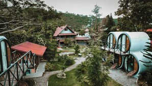 A unique accommodation with a house and cylindrical cabins, surrounded by lush greenery and a garden path.