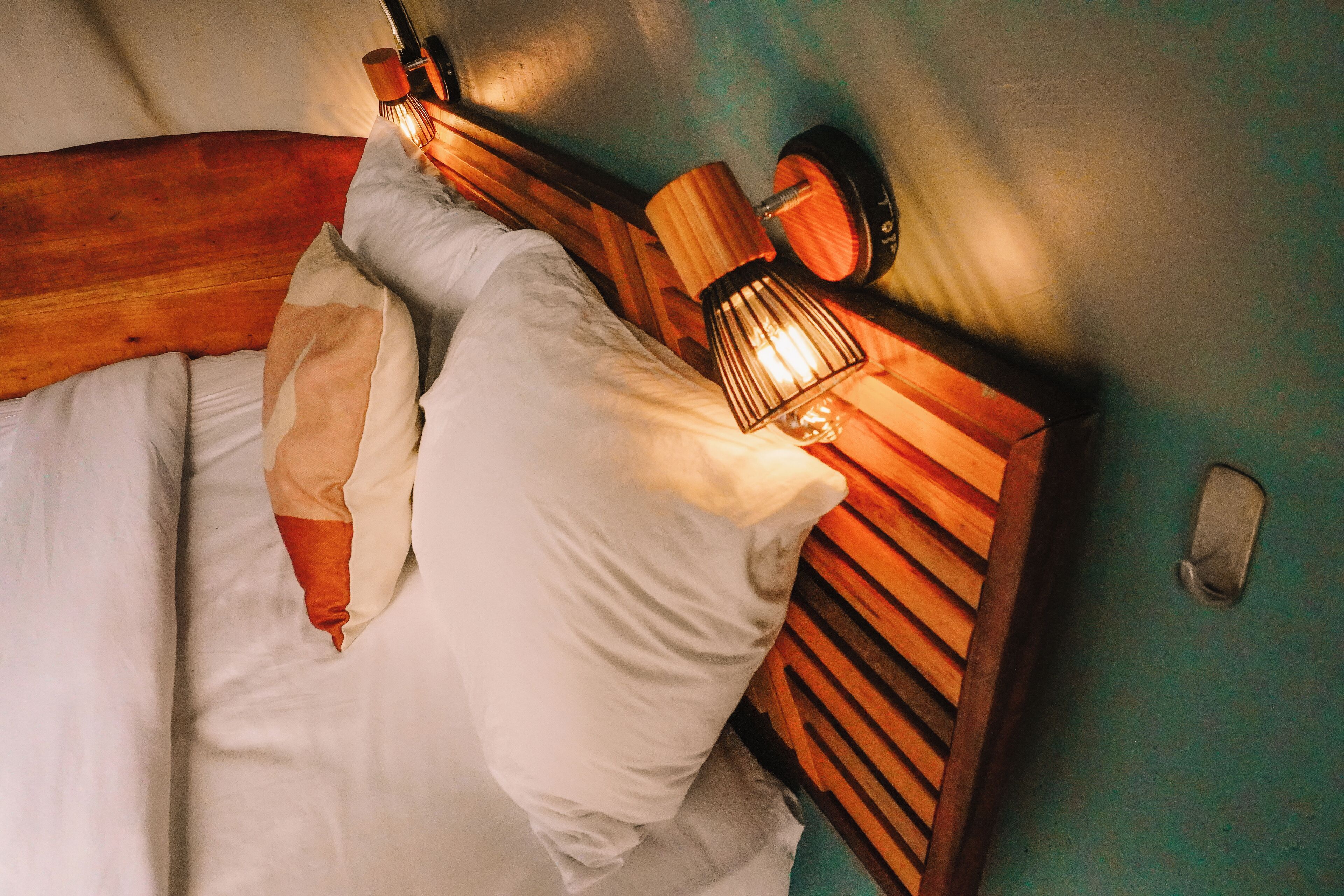Een bed met witte lakens en een houten hoofdbord met een ingebouwde lamp.