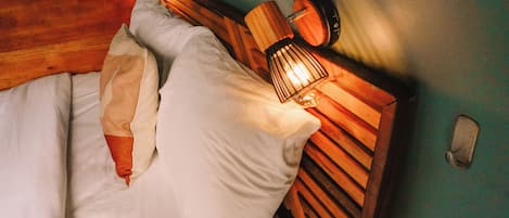 Un lit avec du linge de lit blanc et une tête de lit en bois dotée d’un luminaire intégré.