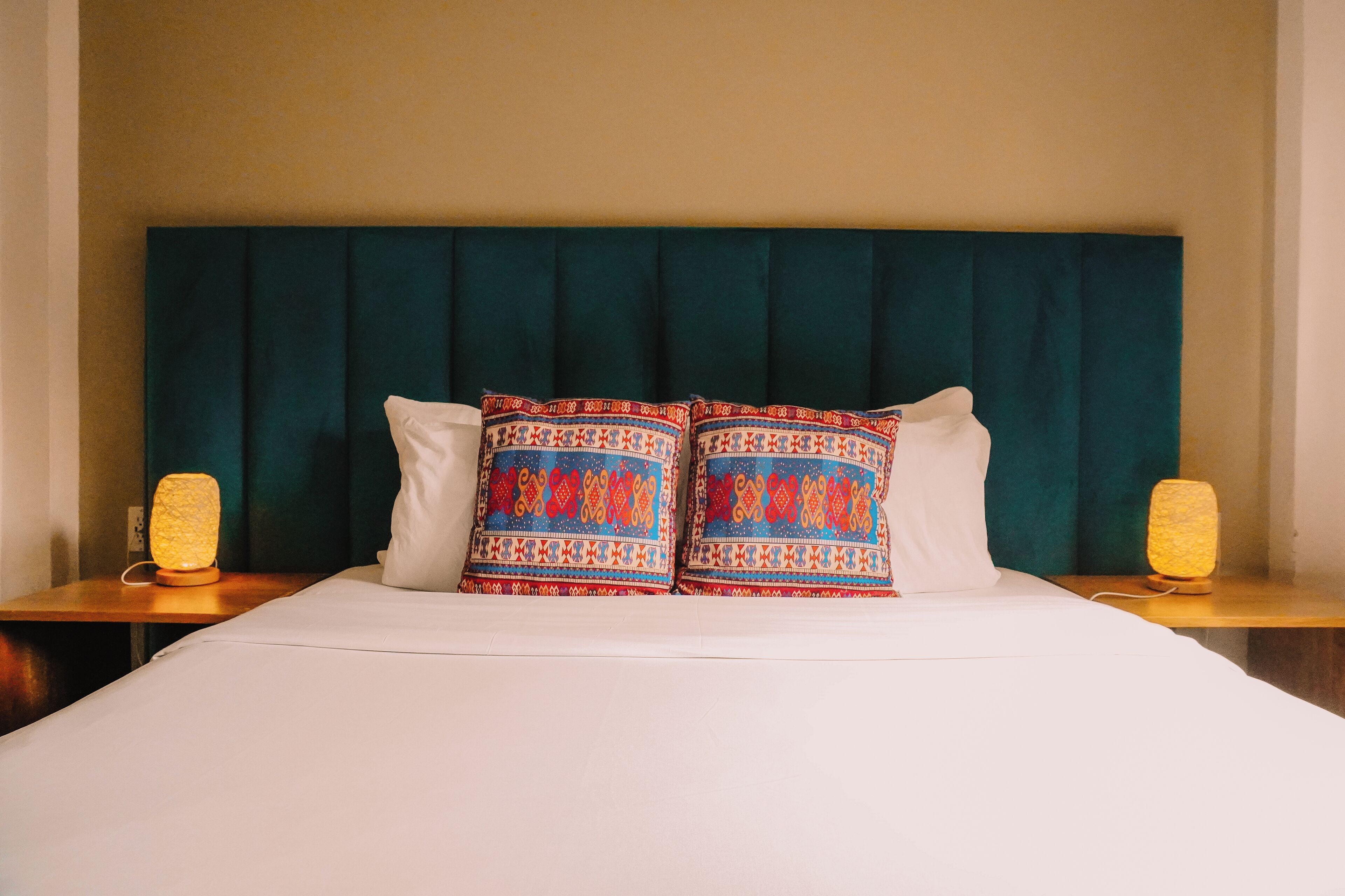 A bed with a teal headboard, two patterned pillows, and two bedside lamps.