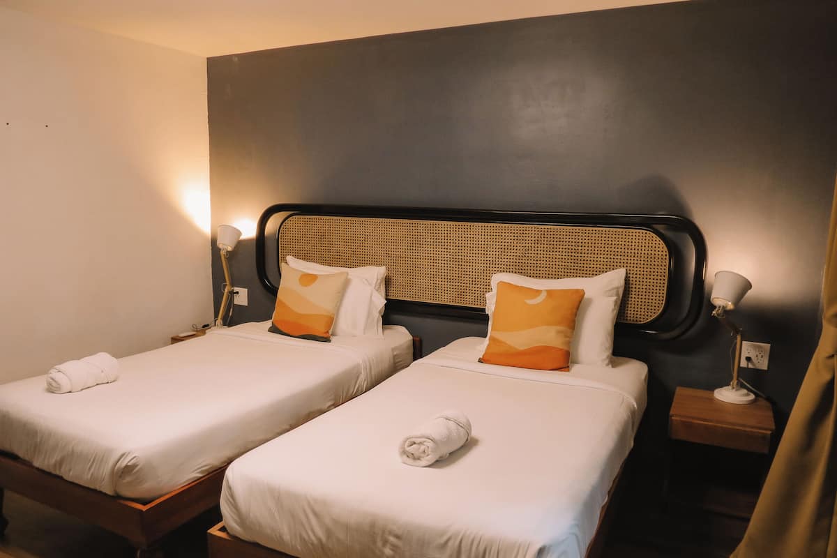 Two single beds with white linens, a woven headboard, bedside lamps, and a wooden nightstand.