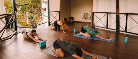 Una clase de yoga en una habitación amplia con suelo de madera y ventanas grandes.