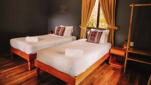 Two wooden beds with white linens and patterned pillows, a wooden nightstand, and a window with curtains.