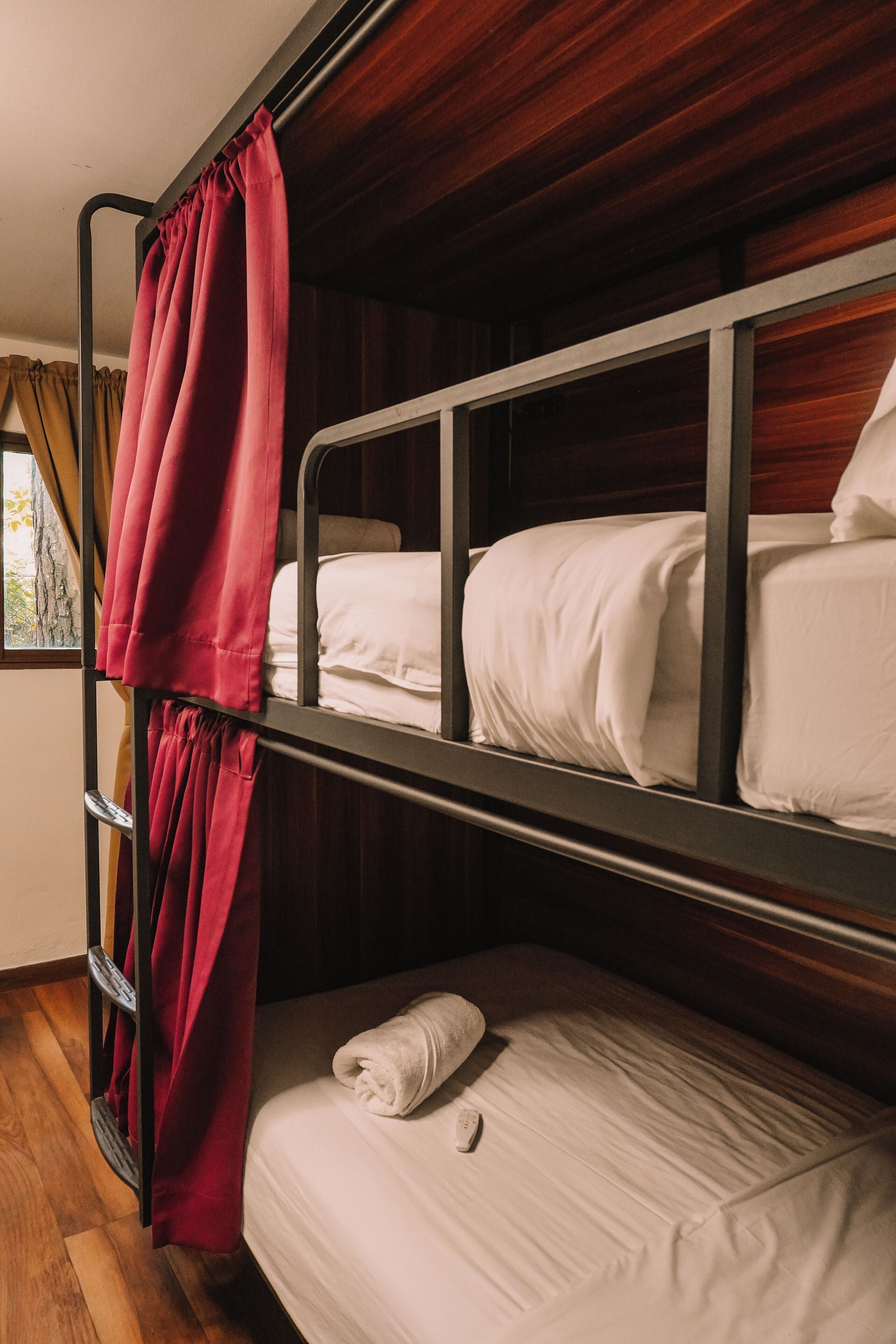 Une chambre avec un lit superposé, un rideau rouge, des murs en bois et une fenêtre également dotée de rideaux.