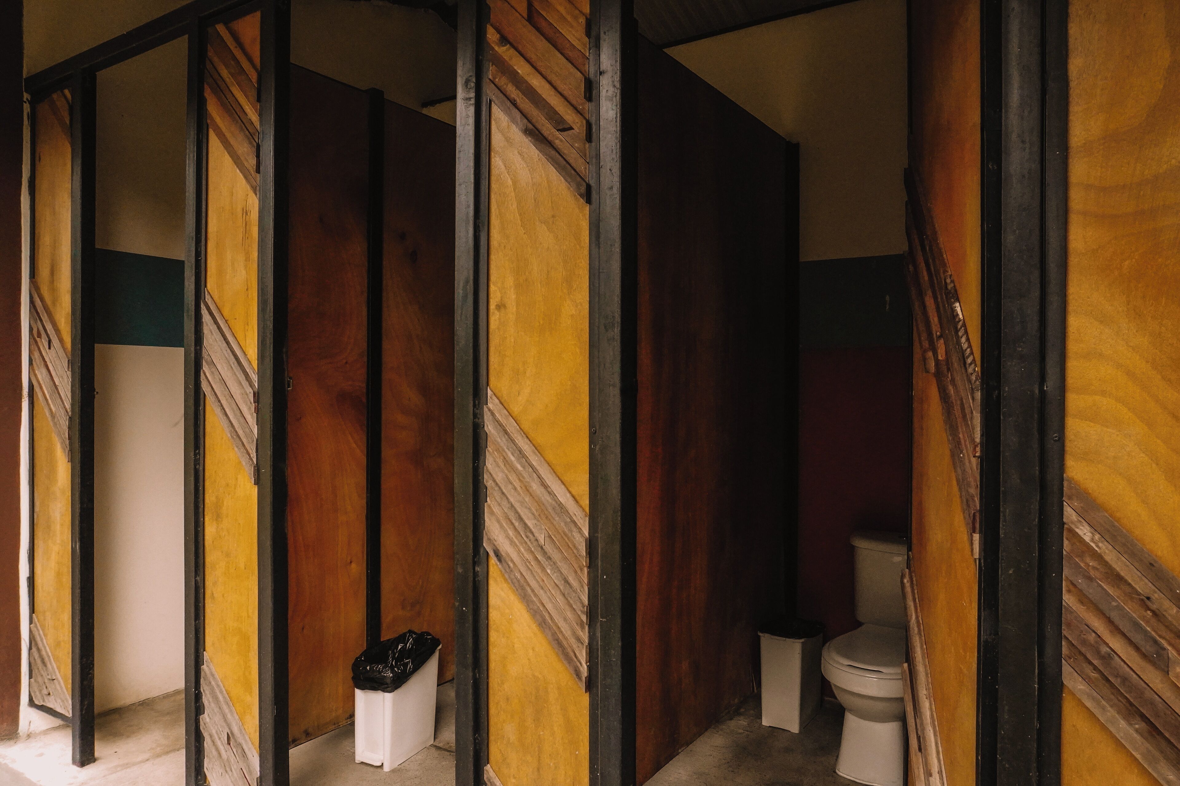 Des toilettes publiques avec des cloisons en bois et des cuvettes de couleur blanche.