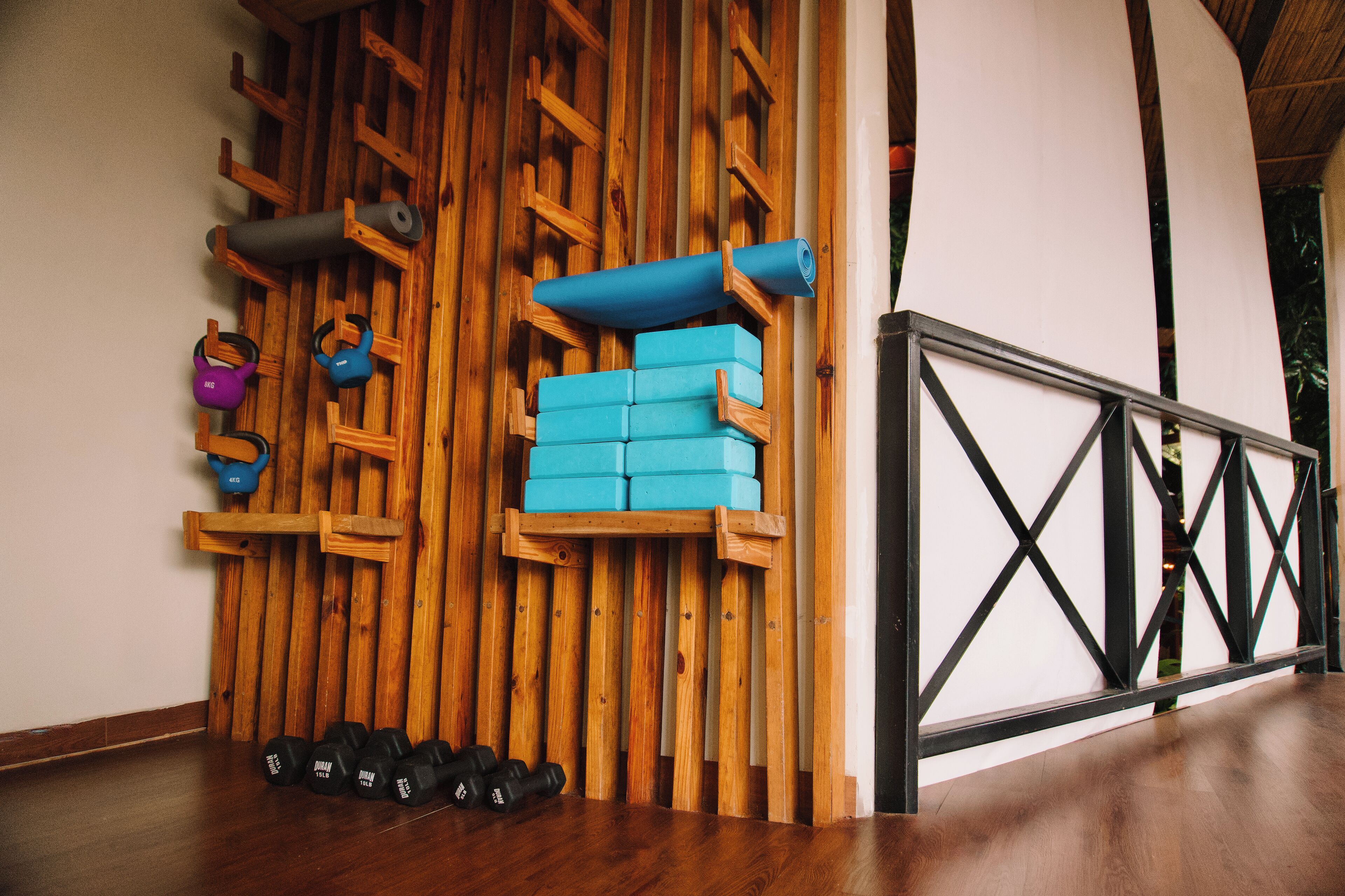 Un gimnasio con paredes de madera, colchonetas de yoga azules, pesas de kettlebell y mancuernas.
