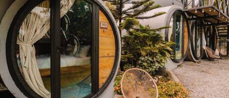 A unique spherical building with a wooden interior, a number '203' on the door, and a small garden area with a chair and plants.