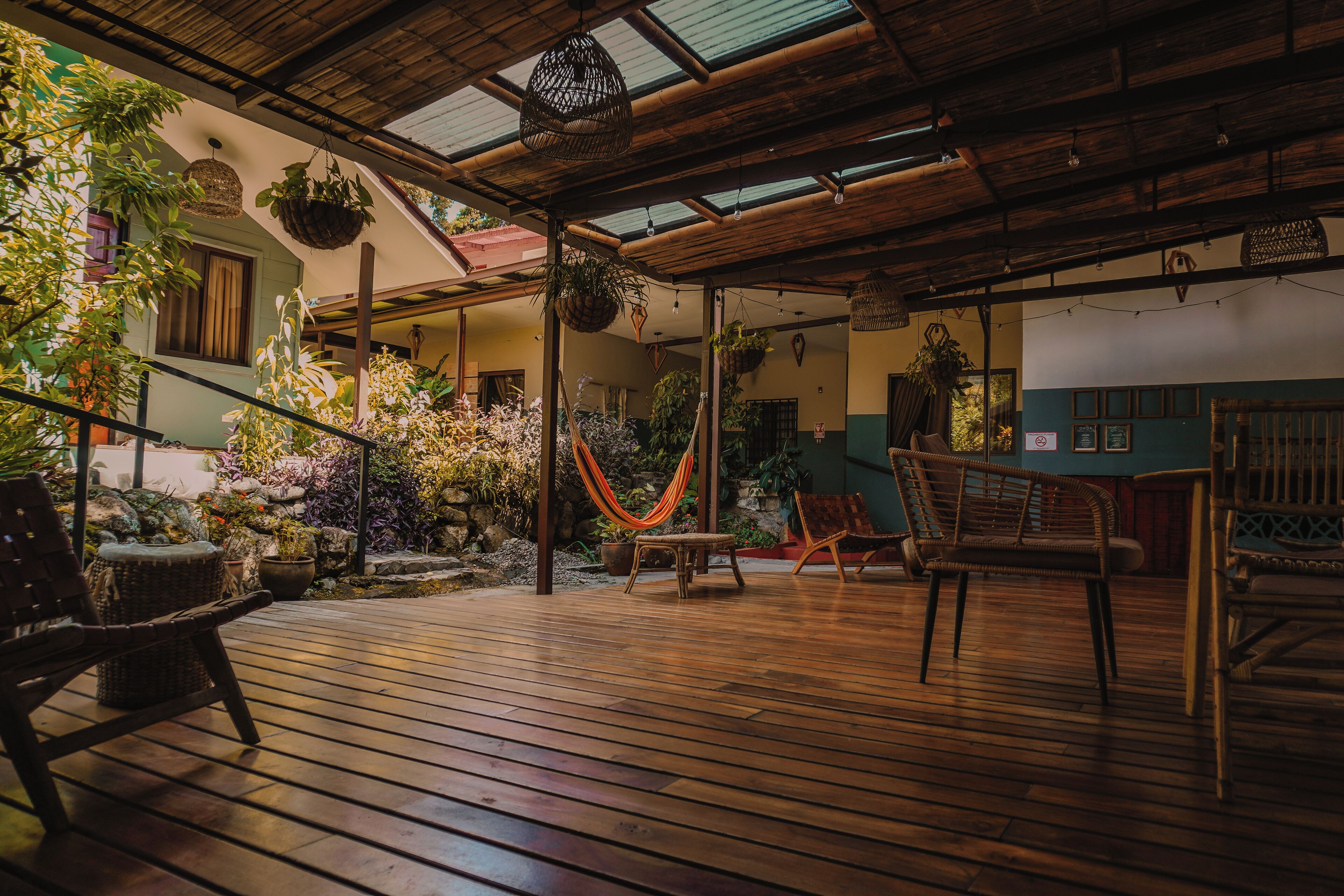 Una terraza de madera con muebles de mimbre, plantas colgantes y una hamaca.