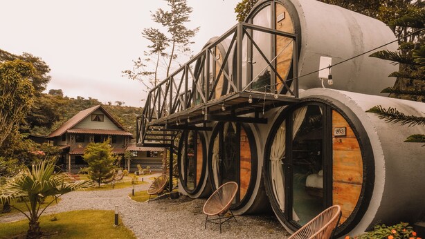 A unique building with large cylindrical structures, a wooden deck, and outdoor seating.