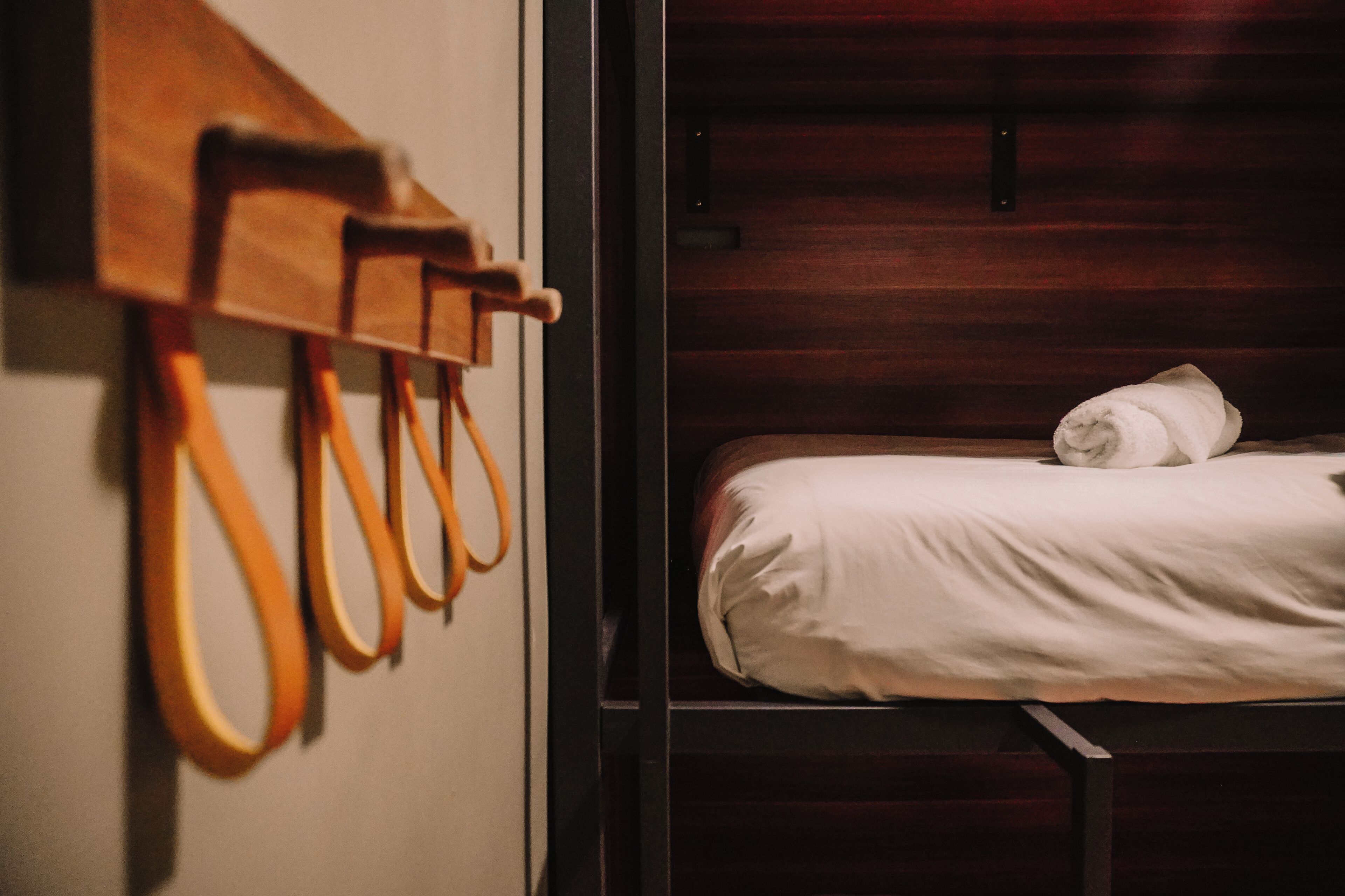 A hotel room with a bed, a wooden coat rack, and a wooden headboard.