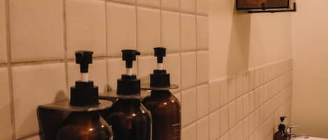 A bathroom with white tiled walls, a white toilet, and three brown dispensers on a wall-mounted shelf.