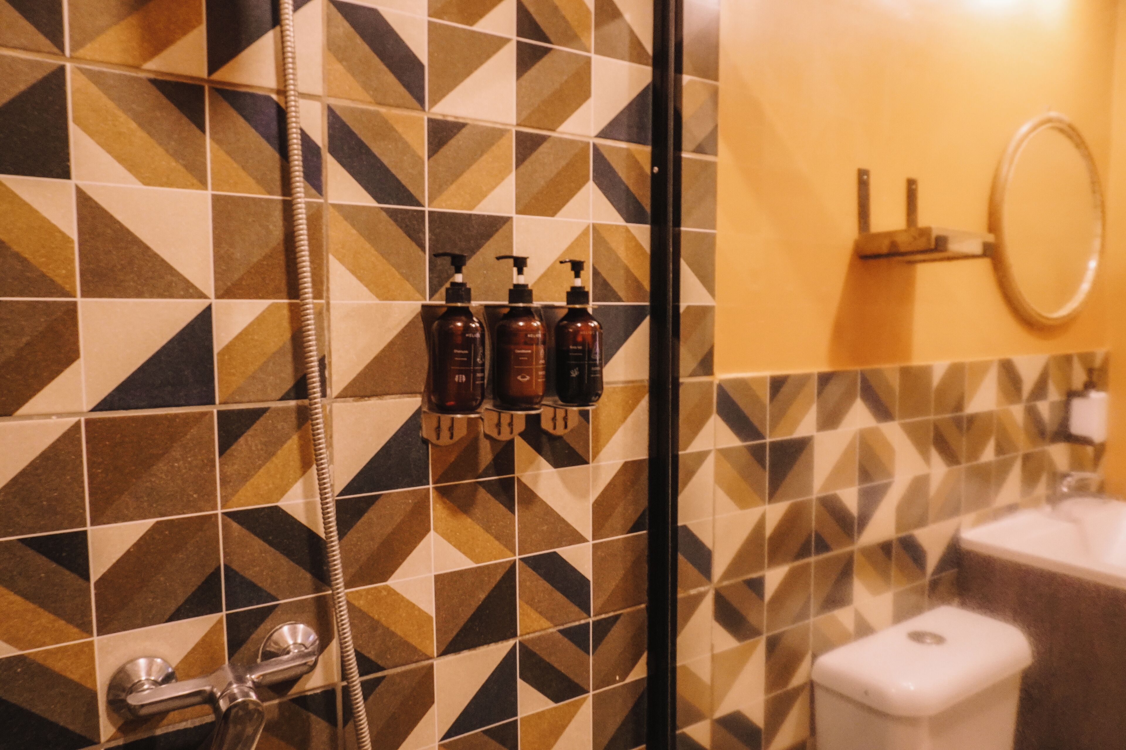 Un baño con un patrón geométrico de azulejos, una ducha, un lavamanos y tres botellas de champú.