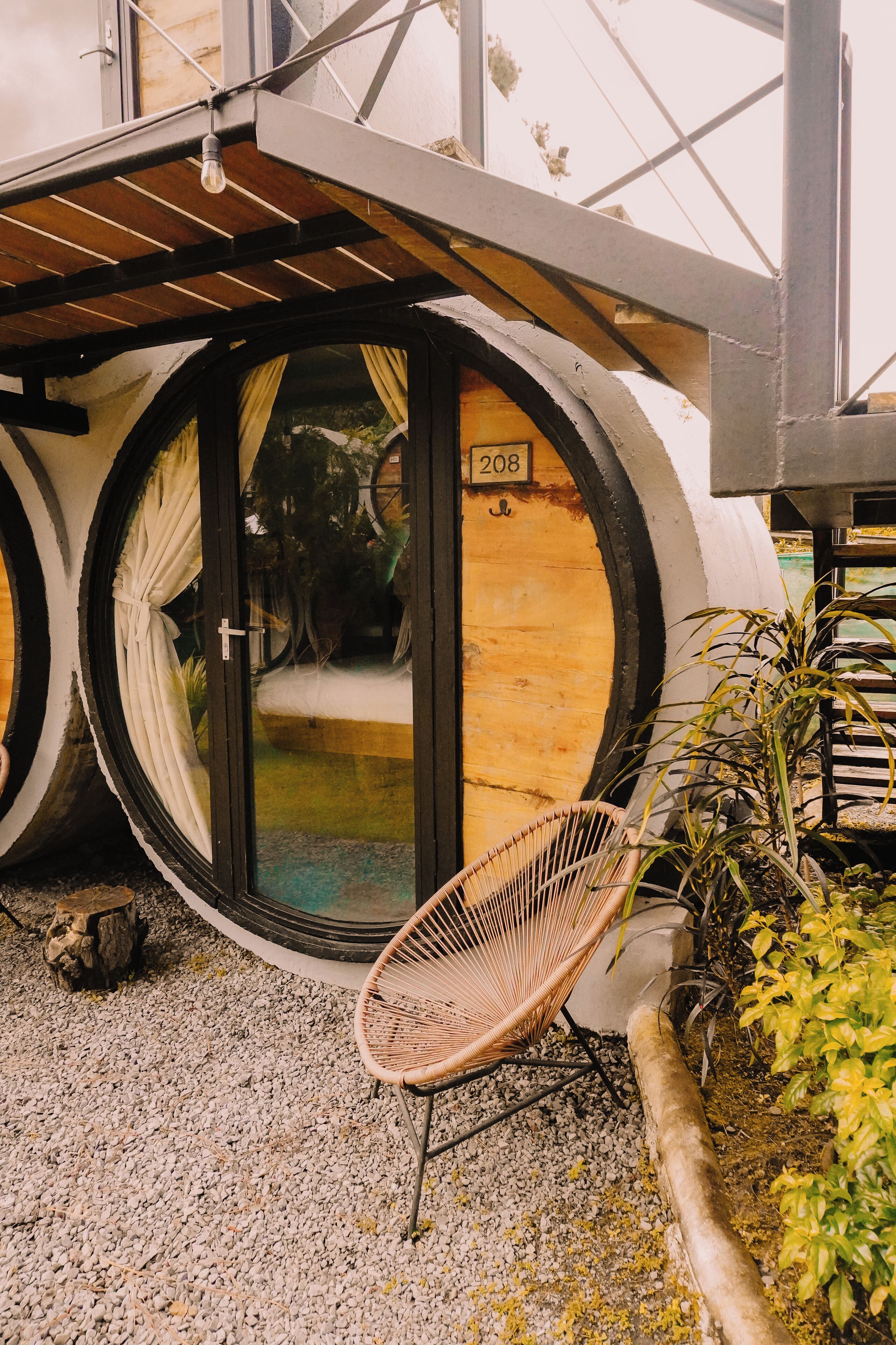 A building with a unique circular window design, a number '208' on the door, and a wicker chair outside.