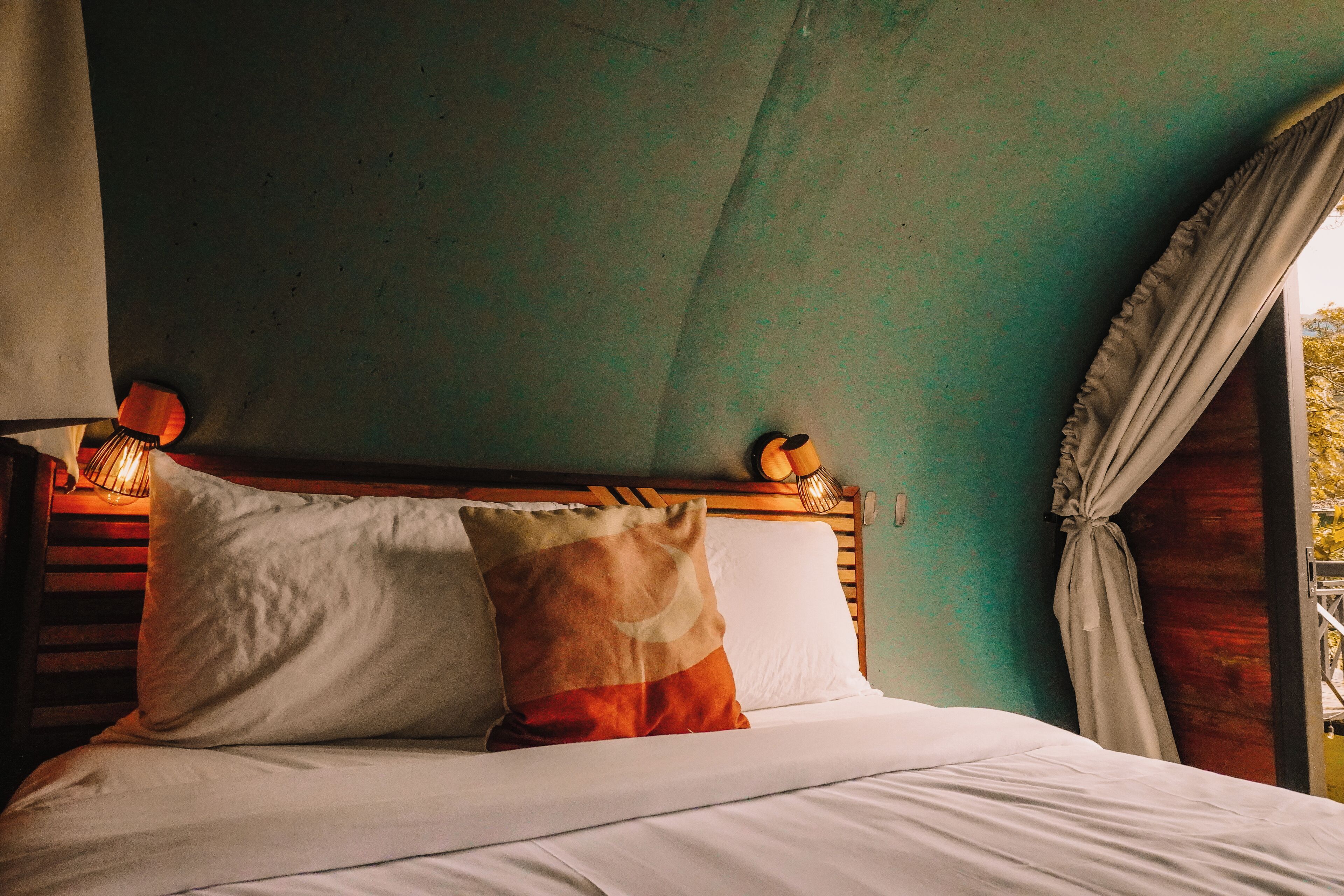 A bed with white and patterned pillows, a wooden headboard, and a green wall.