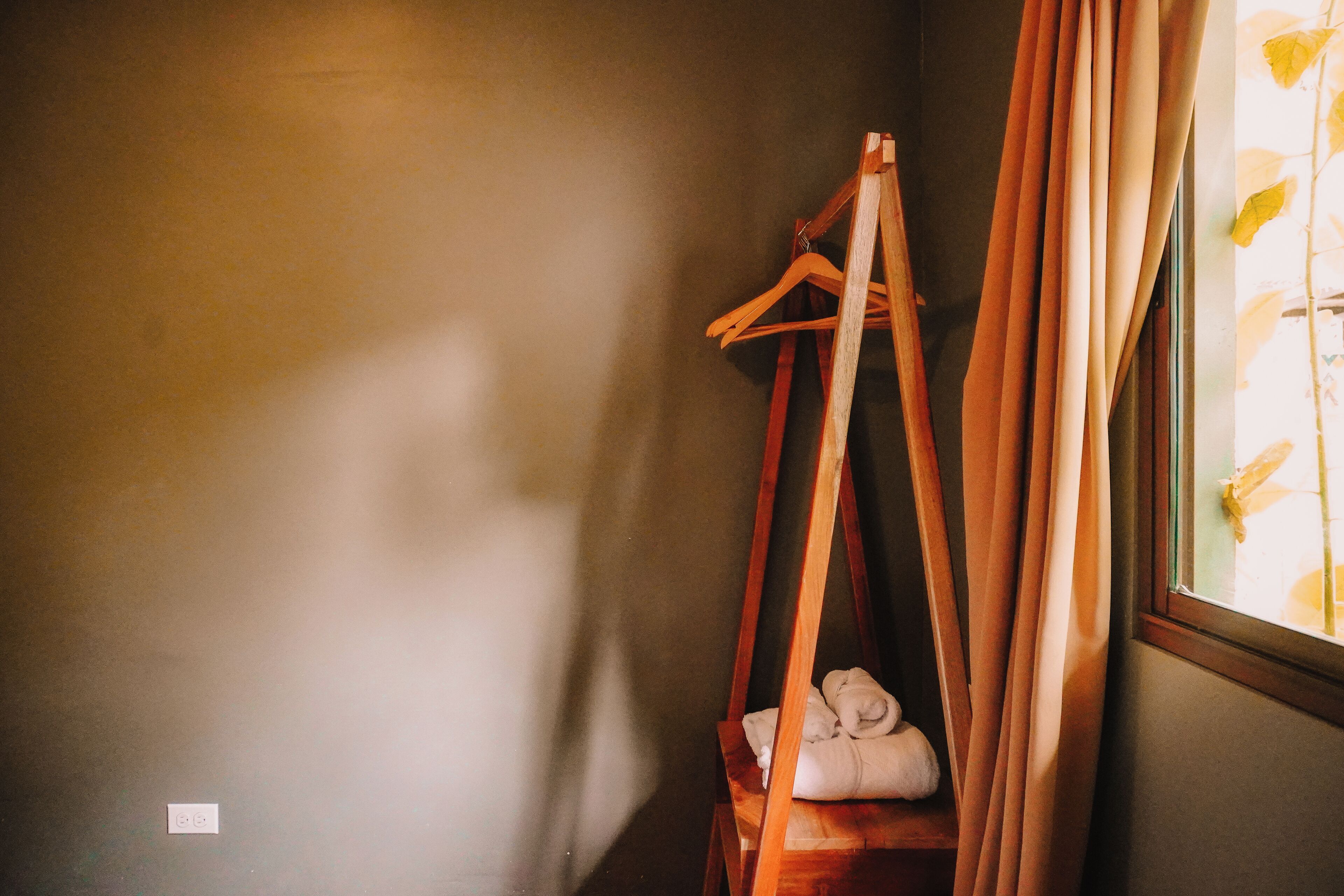 A corner of a room with a wooden hanger and a window with curtains.