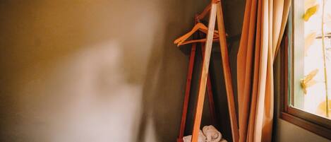 A corner of a room with a wooden hanger and a window with curtains.
