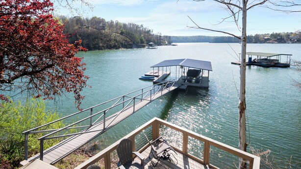 Un lago con barcos amarrados, una terraza de madera con sillas y una vista despejada de los árboles circundantes.