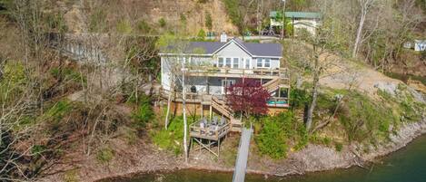 Une maison avec un quai qui s’avance sur un lac, entourée d’arbres et d’une colline.