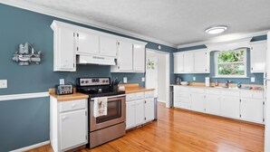 Una cocina con armarios blancos, una estufa de acero inoxidable y una encimera de madera.