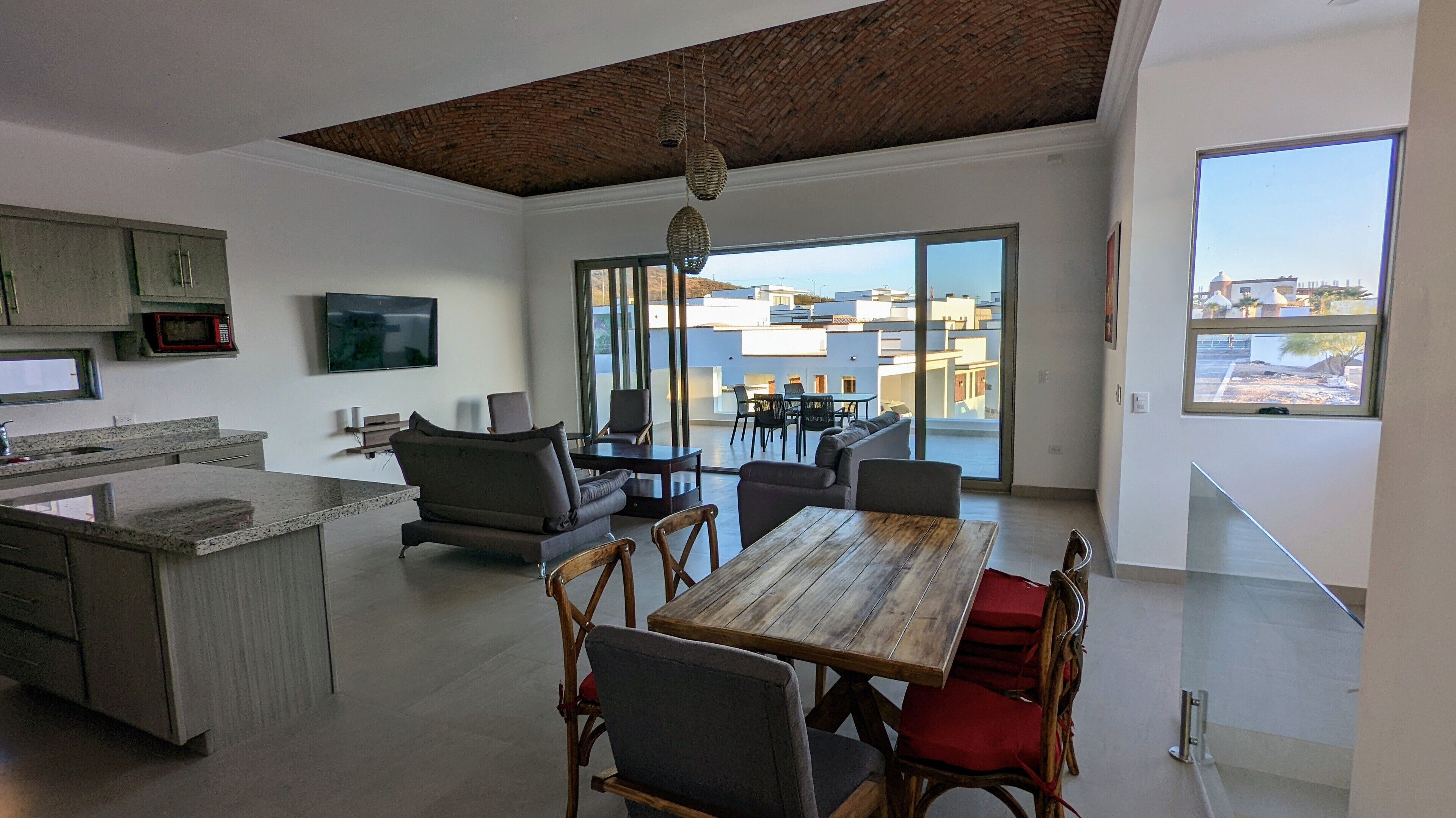 Eine moderne Küche mit Flachbildfernseher, ein Essbereich mit Holztisch und -stühlen sowie ein Balkon mit Blick auf Gebäude.