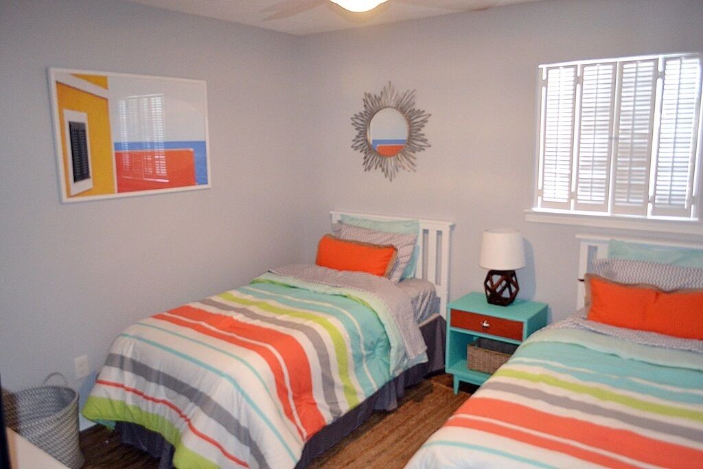 A bedroom with two beds, a nightstand, a mirror, and a window with blinds.