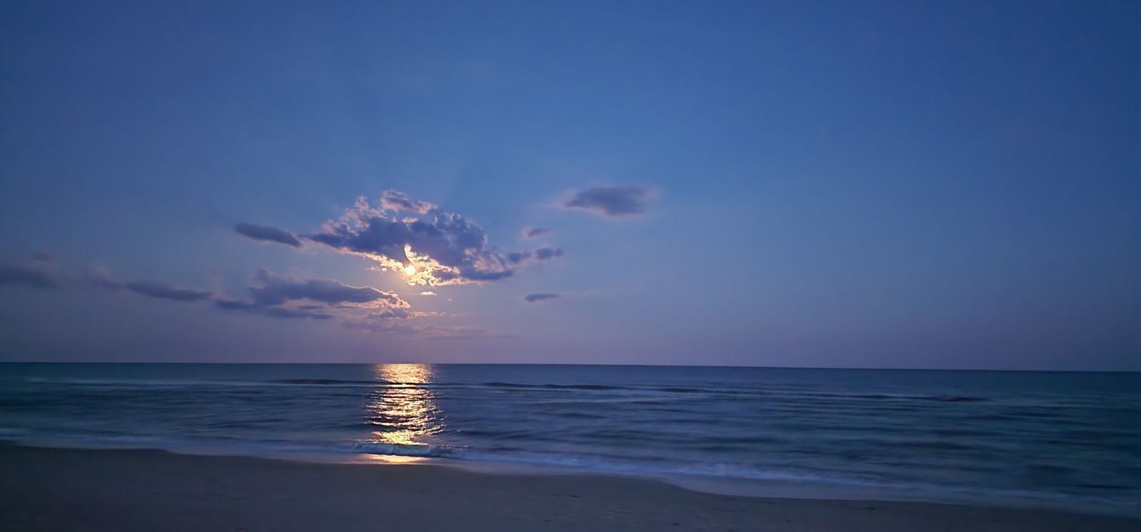 A beach at sunset with the sun reflecting on the water.