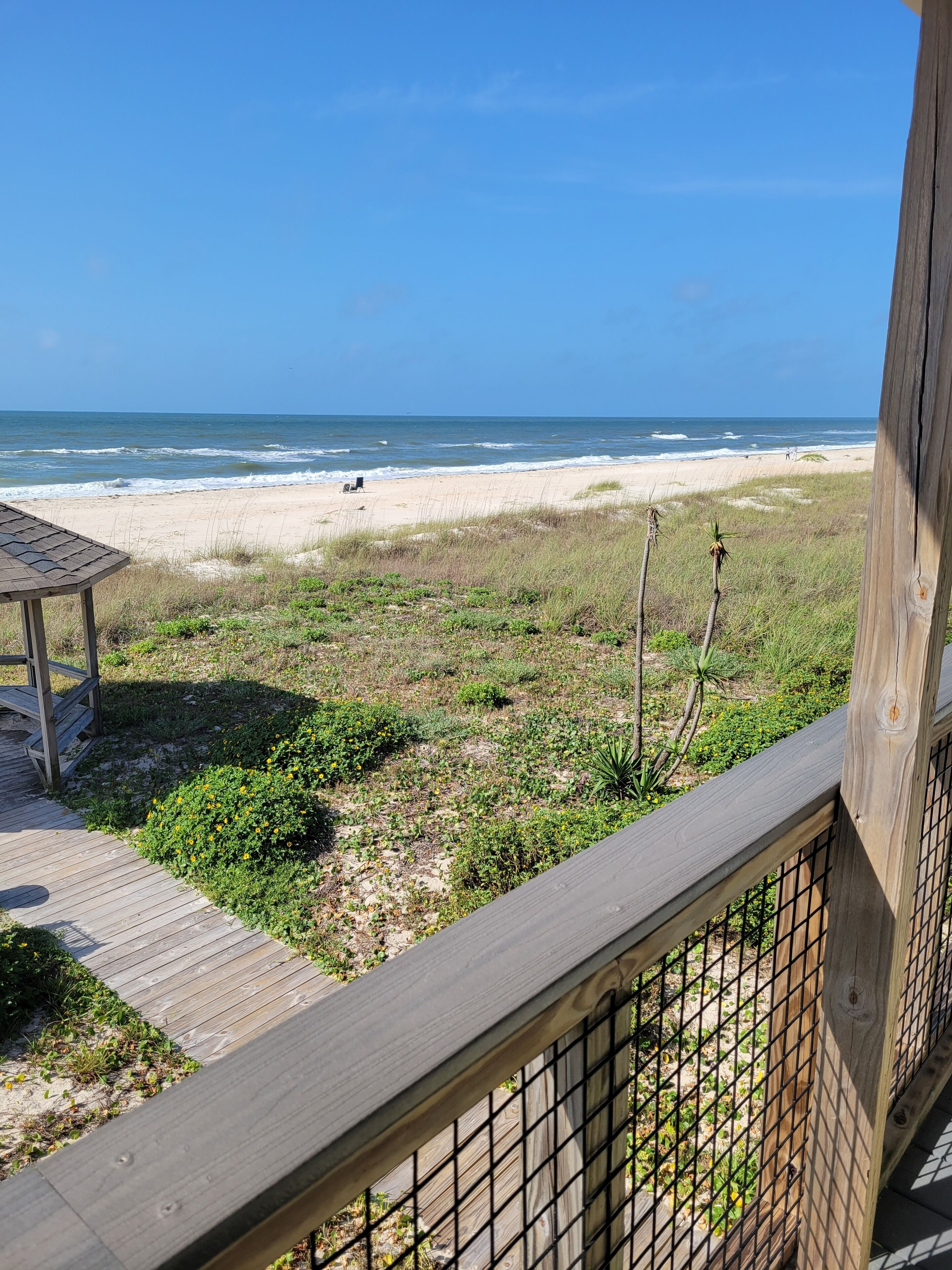 A wooden deck with a view of the beach and ocean.