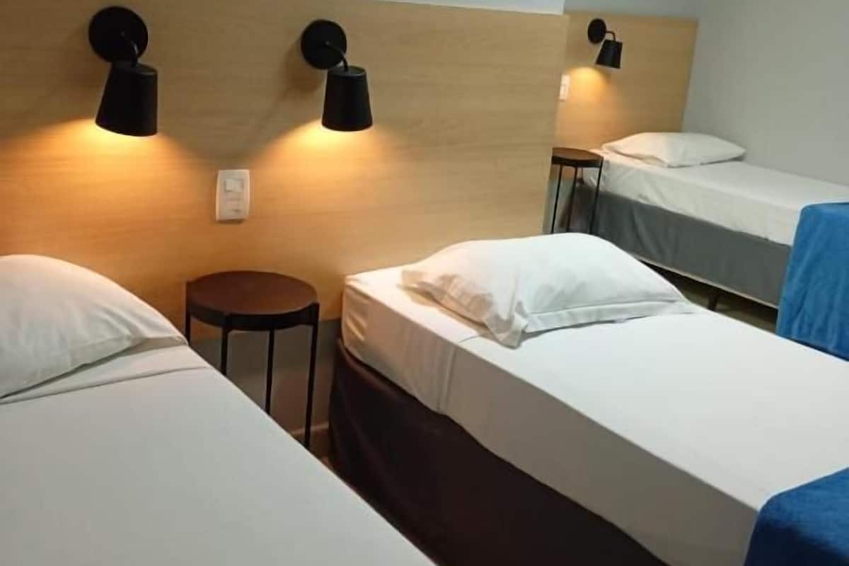 A hotel room with two single beds, a small round table, and wall-mounted lamps.