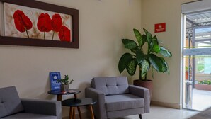 Zona de recepción con dos sillones grises, una mesita, una planta en maceta y una obra de arte enmarcada en la pared.