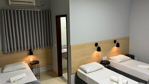 Habitación de hotel con dos camas, cabecero de madera, espejo, mesita y aire acondicionado instalado en la pared.