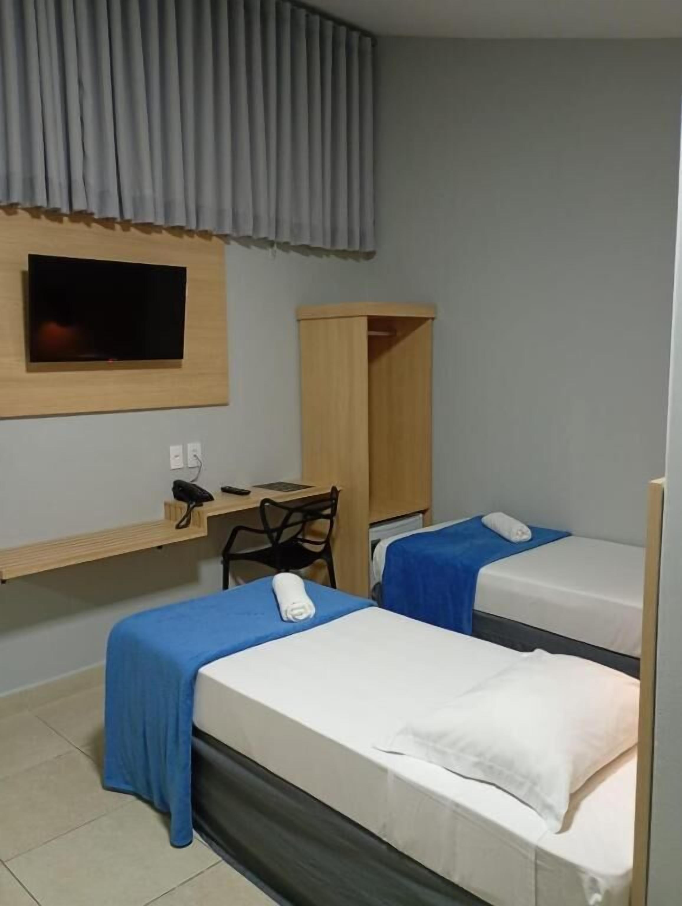 Habitación de hotel con dos camas, un escritorio, una silla, un televisor y un armario.