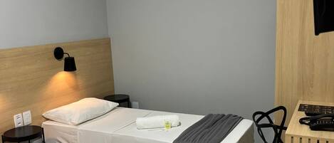 A hotel room with two beds, a desk, a chair, a TV, and a wall-mounted lamp.