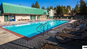 A swimming pool with lounge chairs, a building with a green roof, and trees in the background. - Ski In Ski Out Stagecoach Lift at Heavenly 3BR 3BA (Stateline)