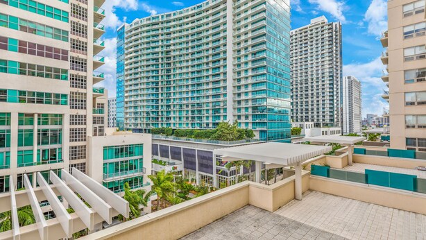 Un edificio moderno de gran altura con varios balcones y una terraza en la azotea con zonas de estar.
