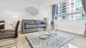 Una sala de estar moderna con un sofá gris, una mesa de centro de vidrio y una zona de comedor con una mesa y sillas de vidrio.