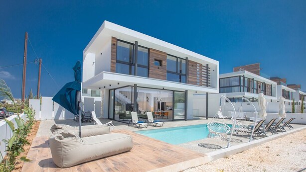 Et moderne hus i to etager med swimmingpool, udendørs møbler og en velplejet have.