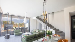 En moderne stue med spiseplads, trappe og et fjernsyn i baggrunden.