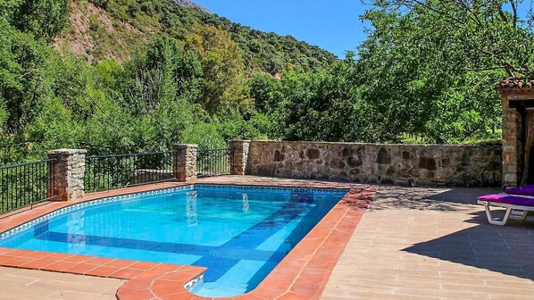 Ein rechteckiger Swimmingpool mit einer gefliesten Kante, umgeben von einer Steinmauer und einem Metallzaun.