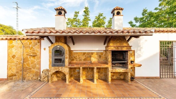 An outdoor kitchen with a stone facade, a built-in oven, and a grill area. - Casa Rural La Garrida Almodóvar del Río by Ruralidays (Córdoba)