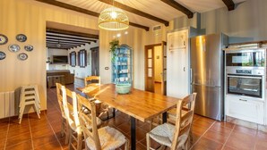 A modern kitchen with a wooden dining table, chairs, a hanging light fixture, and stainless steel appliances. - Casa Rural La Garrida Almodóvar del Río by Ruralidays (Córdoba)