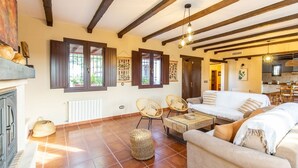 A cozy living room with a fireplace, wooden beams, and a dining area with a table and chairs. - Casa Rural La Garrida Almodóvar del Río by Ruralidays (Córdoba)