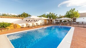 A rectangular swimming pool with a clear blue water surface, surrounded by a brick deck. There are lounge chairs and umbrellas along the poolside, and a white building with a tiled roof in the background. - Casa Rural La Garrida Almodóvar del Río by Ruralidays (Córdoba)