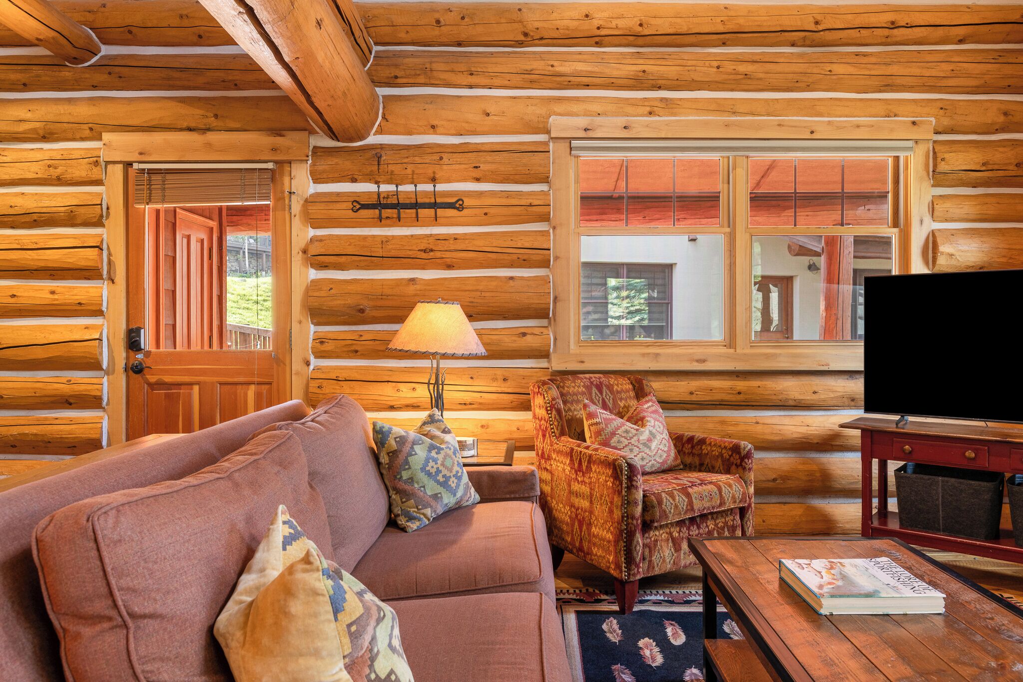 A log cabin interior with a sofa, armchair, lamp, and a television on a wooden table.