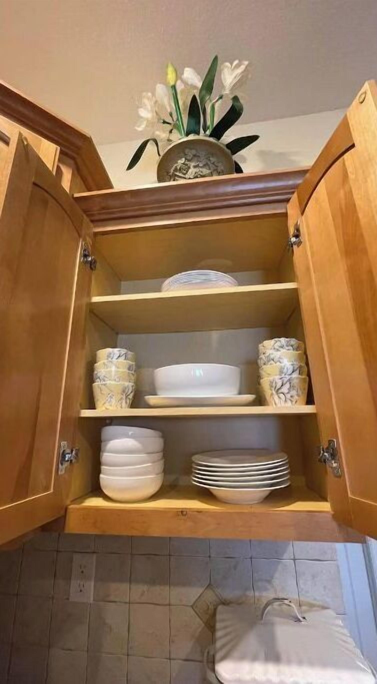 Ein Holzkabinent mit Regalen, auf denen weiße und gemusterte Schüsseln, Teller und eine Blumenvase stehen.