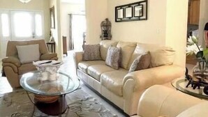 Un salon avec un canapé beige, une table basse en verre et un ventilateur de plafond.