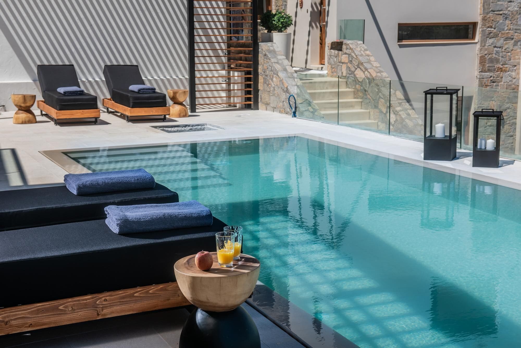 Un espace piscine intérieur moderne, avec des chaises longues, un saladier en bois rempli de fruits et de boissons, et un escalier en pierre.