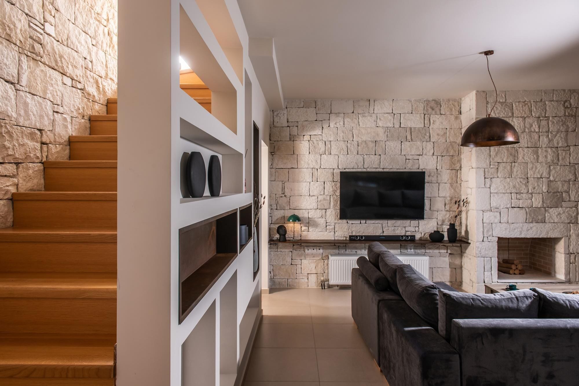 Una sala de estar moderna con una pared de piedra, un televisor de pantalla plana, una chimenea y una escalera con escalones de madera.