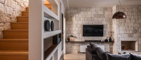 Una sala de estar moderna con una pared de piedra, un televisor de pantalla plana, una chimenea y una escalera con escalones de madera.