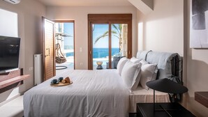 A hotel room with a bed, a TV, a wooden desk, and a view of the ocean. - Alpha House in Crete (Malevizi)