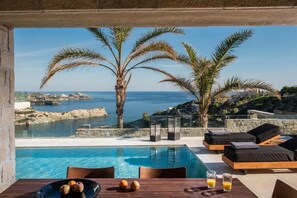 Ein Poolbereich mit Blick auf das Meer, Palmen und eine Steinmauer.